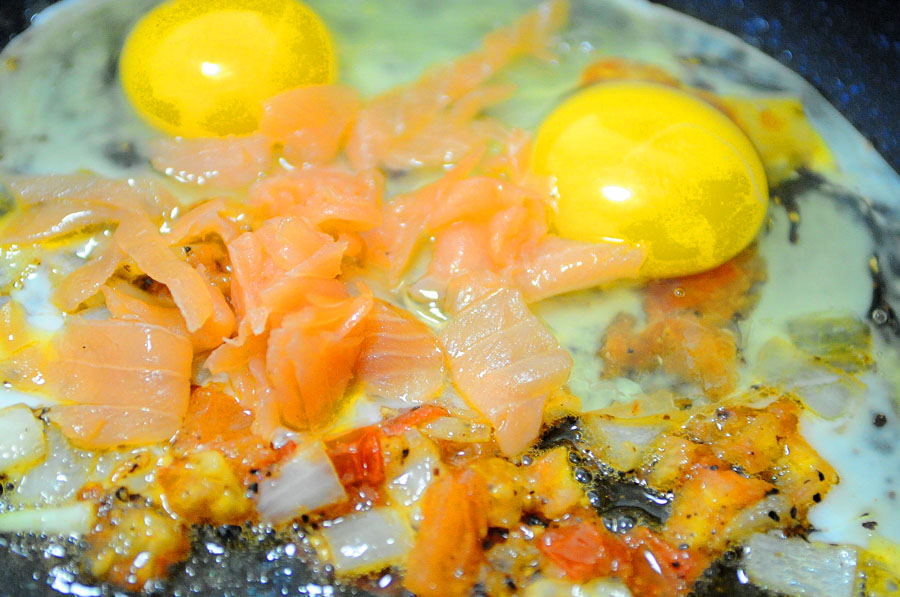 Eggs and lox are added to sauteed onion and tomato for Passover breakfast.